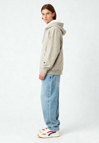 Felpa grigia con cappuccio foderato di peluche, tasca a marsupio; abbinata a jeans blu chiaro e scarpe bianche con accenti rossi e blu.