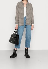 Czarna skórzana torba o strukturalnym designie z złotym akcentem, zestawiona z wełnianą kratkowaną koszulą overshirt, białym topem i jasnoniebieskimi, wysokim stanem jeansami.