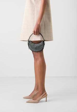 Borsa a mezzaluna nera con decorazioni strutturate, manico piccolo e dettagli metallici. Indossata con una gonna a quadri beige e tacchi nudi.