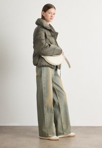 Oliven grønn puffjakke, oversized passform, høy krage; lys beige crossover bag; vide denimjeans med falmede blå og gule nyanser.