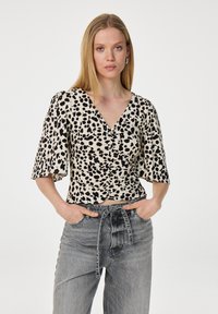 Een blouse met luipaardprint, korte uitlopende mouwen, V-hals en ruches. Gestyld met grijze high-waisted jeans voor contrast.
