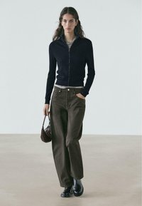 Navy ribbed zip-up cardigan, gray t-shirt, brown wide-leg trousers, black ankle boots, and a small brown handbag.