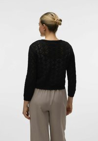 Maglione corto nero lavorato a maglia con un motivo ondulato testurizzato, dotato di maniche a tre quarti e scollatura rotonda. Indossato con pantaloni beige.