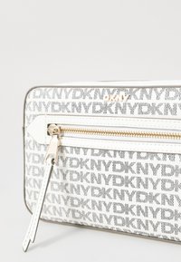 Clutch bianco con zip, caratterizzato da un motivo con logo DKNY, hardware metallico, texture liscia e una forma rettangolare elegante. Zip dorata in evidenza.