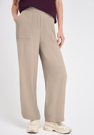 Pantalon beige à jambes larges avec taille élastique et poches avant, porté avec des baskets blanches et un haut violet foncé.