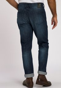 Jeans de mezclilla azul oscuro con un ajuste ajustado, puños doblados y una etiqueta de cuero negra en la cintura. Cuenta con dos bolsillos traseros.