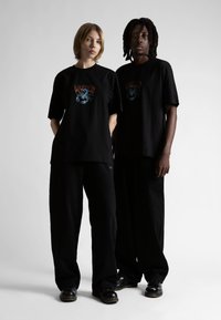 Melnas pārāk lielas T-kreklus rotā skorpiona attēls ar uzrakstu "Wasted". Abi modeļi valkā brīvus melnus bikses un melnas kurpes.