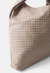 Beige gewebte Handtasche mit einer weichen Textur, die ein charakteristisches Korbmuster und eine abgerundete, lässige Form aufweist.
