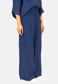 Pantalons larges bleu marine en tissu crêpé texturé avec une taille élastique. Présente un cordon de serrage et une coupe décontractée.