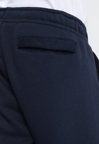 Marinblå sweatpants har ett strukturerat tyg, elastisk midja och en diskret bakficka för förvaring.