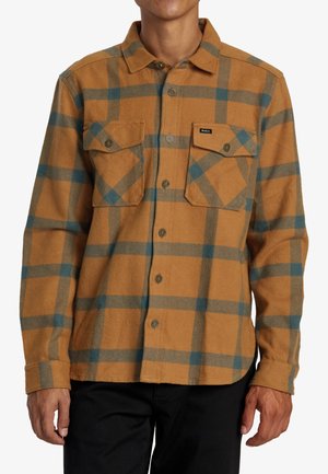 Brown flannel shirt with blue checkered pattern, two chest pockets, and button closure. Soft texture, long sleeves, and rounded hem.