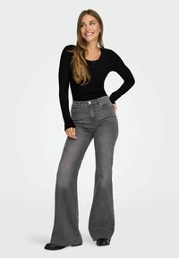 Zwarte geribbelde lange mouwen top gecombineerd met grijze flared jeans. De jeans hebben een klassiek vijf-pocket ontwerp en een knoopsluiting.