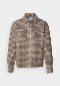 Chaqueta de cuadros marrón y beige con cremallera, dos bolsillos en el pecho y cuello extendido, exhibida sobre un fondo blanco.