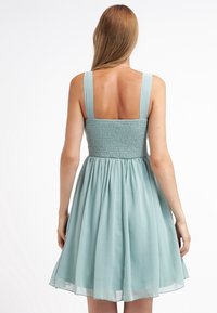 Světle modro-zelené bezramenné šaty se smockovaným živůtkem a plnou sukní, vyrobené z lehké látky. Hladká textura a střední délka.