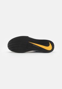 Sole di scarpa sportiva nera con un motivo a spina di pesce, caratterizzata da un logo Nike arancione e un bordo superiore liscio.