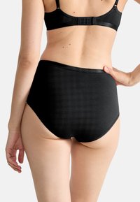 Culotte taille haute noire en tissu lisse, avec un design sans coutures, une brillance subtile et une ceinture élastique.