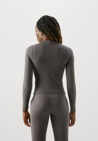 Tailliertes Langarmshirt aus dunkelgrauem Material, mit glatter Textur, Rundhalsausschnitt und dezent gewölbten Nähten. Kombiniert mit passenden Leggings.
