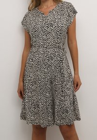 Czarna sukienka z krótkim rękawem, z białym wzorem w kropki, dekoltem w serek, zaznaczoną talią i zwiewnym dołem sięgającym do połowy uda.