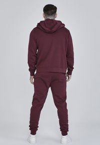Bordeaux hoodie en sweatpants van zacht materiaal, met een trekkoordcapuchon en ribbelmanchetten. Gladde textuur zonder zichtbare patronen.