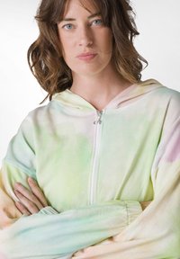 Felpa con cappuccio e zip in colori pastello tie-dye, caratterizzata da una texture morbida, maniche lunghe e polsini elasticizzati.