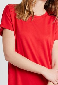 Červené tričko s krátkým rukávem vyrobené z měkké látky, s kulatým výstřihem a volným střihem, hladká textura bez viditelných vzorů nebo akcentů.