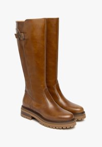 Des bottes en cuir jusqu'aux genoux d'une riche couleur marron, avec une finition lisse, un détail de boucle sur le côté et une semelle épaisse texturée.