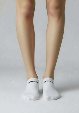 Chaussettes blanches à la cheville avec une texture lisse, ornées d'un logo noir "SIXTH JUNE" sur le bord-côte. Placées sur un fond neutre.