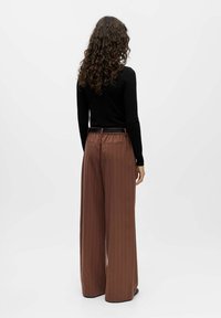 Pantalons larges à rayures marron avec une coupe confortable, ceinture élastique et poches latérales. Le modèle porte un haut à manches longues noir.