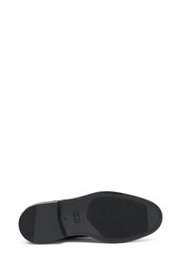 Suela de zapato de goma negra con una superficie texturizada, forma redondeada y refuerzo en el talón. El contorno indica un diseño de construcción sólido.