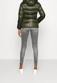 Mörkgrön vadderad jacka med horisontella paneler och huva, kombinerad med grå jeans i smal passform och vita sneakers. Tyg med slät, glänsande yta.