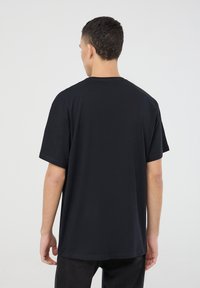 Maglietta nera in cotone con vestibilità comoda, maniche corte e scollatura rotonda, caratterizzata da una texture liscia e un design semplice.