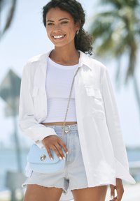 Weißes Hemd über einem weißen, gerippten Crop-Top, kombiniert mit hellblauen Jeansshorts. Accessoires: eine hellblaue, geflochtene Handtasche.