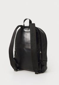 Zwarte leren rugzak met verstelbare stoffen banden, afgeronde vorm, zijvakjes met rits en een bovenste handvat om te dragen. Gladde textuur.