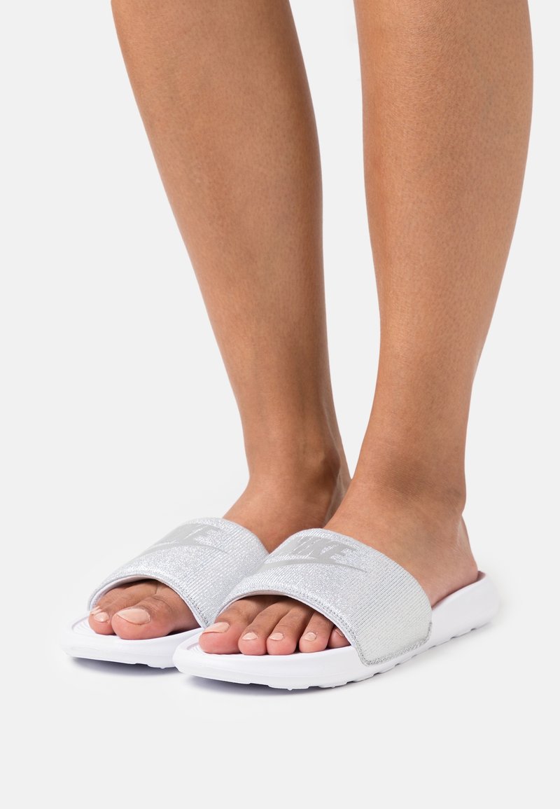 Silverfärgade slidesandaler med en texturerad rem och vit yttersula, med en stor logotyp på ovandelen. Platt design för enkel användning.
