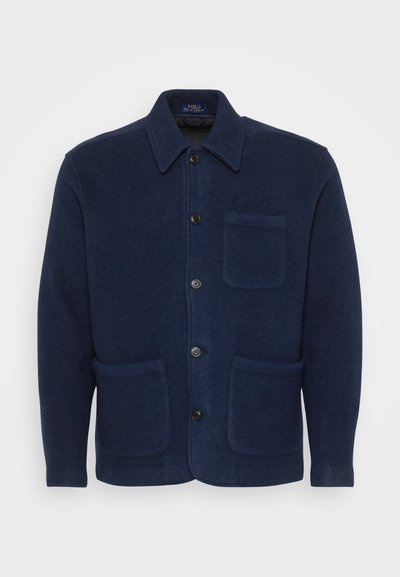 Marinblå ulljacka med krage, framknäppning, två stora sidofickor och en bröstficka. Slät textur.