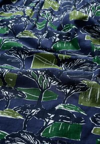 Mönstrad tyg med abstrakta träd i vitt på en marinblå bakgrund med gröna och ljusgröna geometriska former. Predominant bomullstextur.