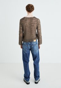 Stickad brun tröja med strukturerade ränder, kombinerad med blå lösa denimjeans och svarta platåskor, sedd bakifrån.