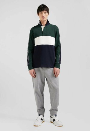 Polo à manches longues rayé en vert, blanc et bleu marine ; il présente un col et une patte de boutonnage. Assorti à un jogging gris et des baskets.