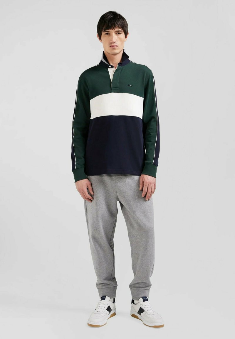 Polo à manches longues rayé en vert, blanc et bleu marine ; il présente un col et une patte de boutonnage. Assorti à un jogging gris et des baskets.