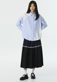 Gestreepte blauwe blouse met kantaccent op één schouder, gecombineerd met een zwarte geplooide rok en zwarte sneakers.