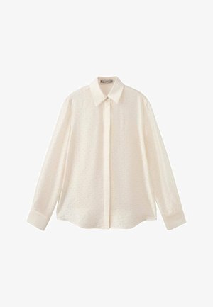 Camisa blanca de manga larga con botones y cuello clásico, con una tela texturizada con pequeños patrones de puntos y mangas abotonadas.