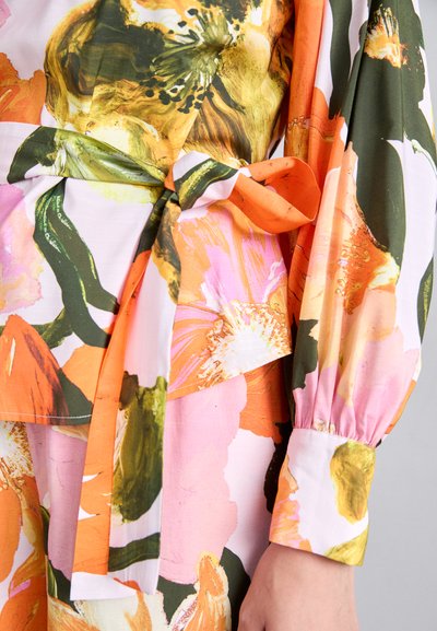 Blusa floreale con motivi vivaci arancioni, rosa e verdi, dotata di vita con cintura e maniche puffate con polsini arricciati.