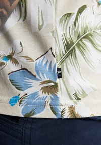 Katoenen stof met bloemenprint met blauwe bloemen en groene bladeren op een beige achtergrond; marineblauwe stof aan de onderkant met stikdetails.