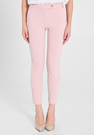 Helle rosa Slim-Fit-Hosen mit glatter Textur, goldener Knopfverschluss und Seitentaschen, kombiniert mit neutralen Absatzschuhen.