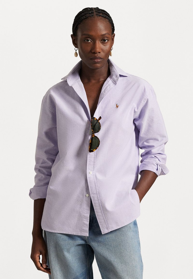 Light purple button-up shirt in a relaxed fit, cotton fabric, with a classic collar and small logo on the chest. Worn with sunglasses.