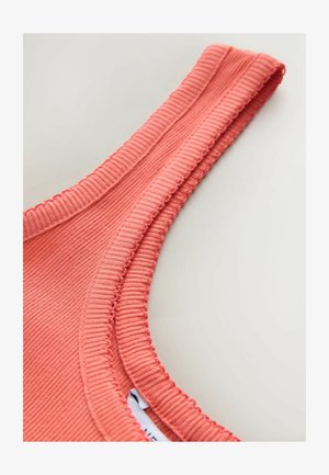 Korallfärgad ribbad tyglinne med rundad halsringning och sydda detaljer längs kanterna, med en inre etikett delvis synlig.