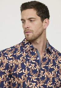 Korte mouwen overhemd met een diepblauwe stof en een oranje bloem- en bladmotief, met een button-down kraag en een contrasterende spijkerstof naden.