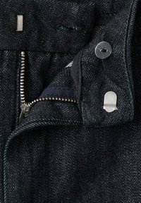 Tissu en denim foncé avec une fermeture éclair visible, des accessoires en argent et une fermeture par bouton. Présente une texture subtile et des coutures contrastées.