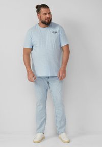 Lichtblauw T-shirt met korte mouwen en een ronde halslijn, voorzien van een klein logo op de borst, gecombineerd met lichte denim jeans en witte sneakers.