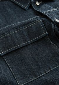 Donkerdenim overhemd met een op maat gemaakte kraag, witte stiksels en een borstzakje. De stof heeft een subtiele textuur en een klassieke pasvorm.